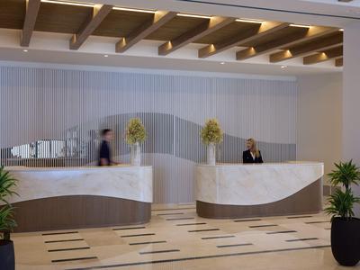 Modern hotel check-in area with curved marble counter and decorative plants.
