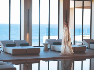 Bright hotel lounge with sofas, large glass windows, and sea view.