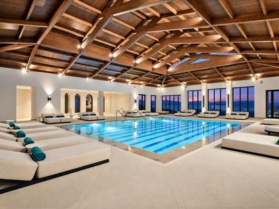 Indoor hotel pool with wooden ceiling and loungers with green cushions.