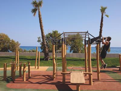 Playground with swings and climbing frame by the sea with palm trees.