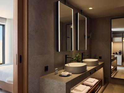 Modern bathroom with double sinks, large mirrors, and access to a bedroom.