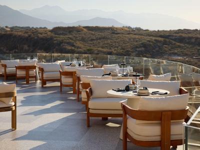 Terrace with wooden chairs and tables overlooking mountains at sunset.