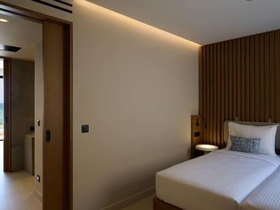 Modern bedroom with white bed, wooden wall, and sea view through open door.