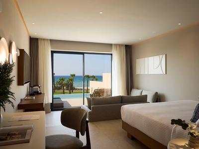 Modern hotel room with large bed, sofa, and view of terrace and sea.