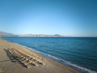 Empty sandy beach with rows of sun loungers and clear blue sky.
