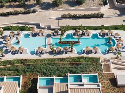 Aerial view of a hotel with a large, curved outdoor pool and sun loungers under umbrellas.