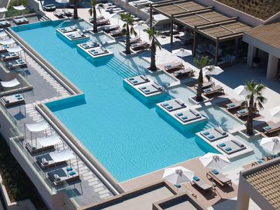 Modern hotel pool with loungers, umbrellas, and covered seating area beside the water.