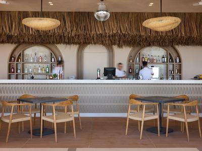 Modern hotel bar area with wooden furniture, round lamps, and decorative counter with drinks.