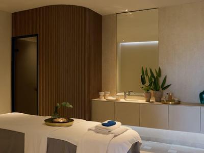 A calm spa room with massage table, plants, and soft lighting.