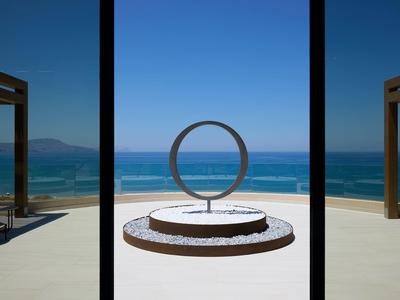 Modern seating area with sculptural circle facing the sea and clear sky.