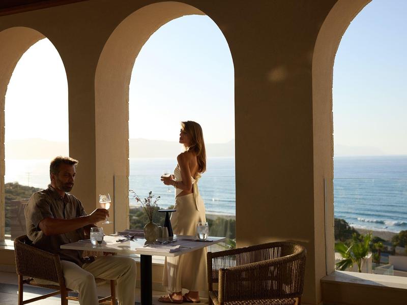 Couple enjoys sunset and wine on balcony overlooking the sea.