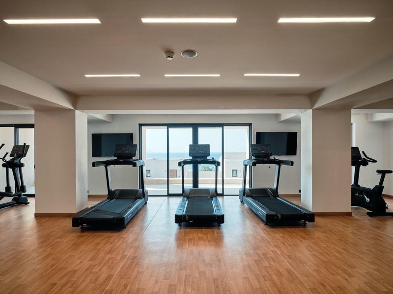 Gym with treadmills facing large windows overlooking the beach and sea.