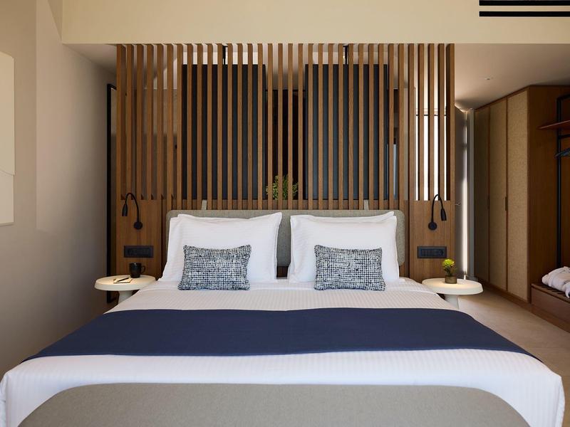 Modern hotel room with double bed, wooden slat wall, and minimalist decor.