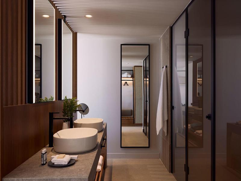 Modern hotel bathroom with sink, large mirror, and wardrobe in the background.