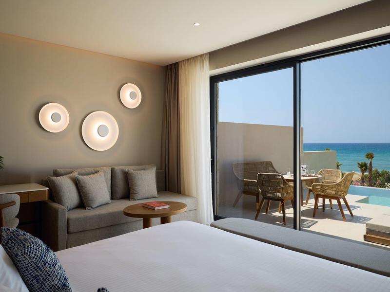 Modern hotel room with balcony, sea view, and cozy seating area.