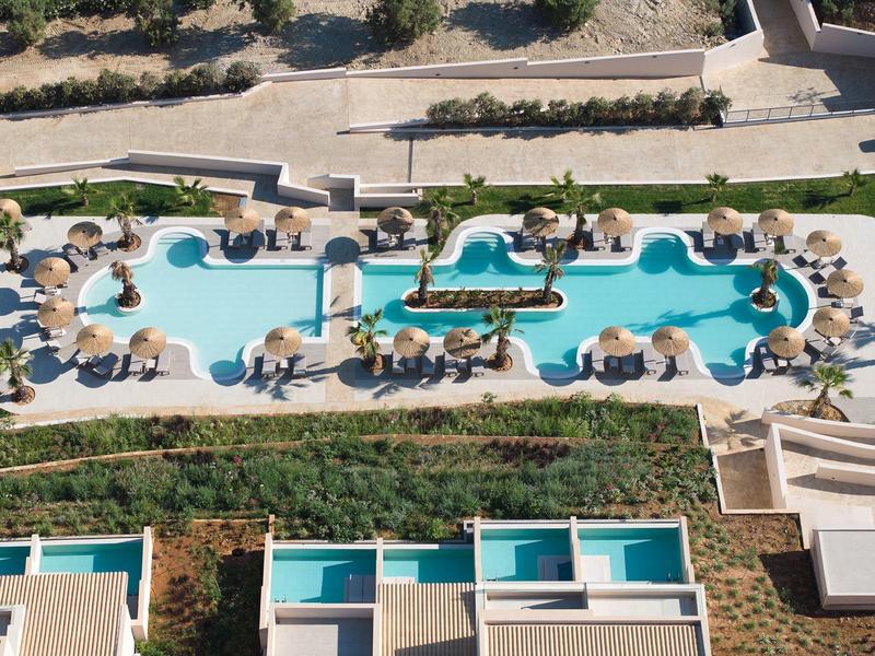 Aerial view of an elongated pool with island and sun umbrellas at a hotel resort.