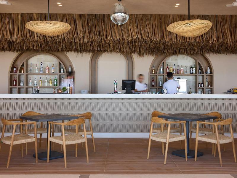 Modern hotel bar area with wooden chairs and decorative bottle shelves behind the counter.