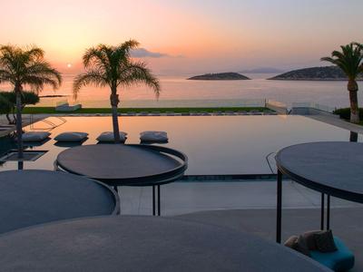 Blick auf einen Pool mit Liegen und Palmen bei Sonnenuntergang am Meer.