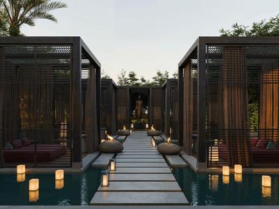 Moderner Gehweg mit Laternen zwischen Pools und offenen Lounge-Bereichen bei Dämmerung.