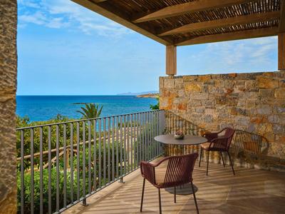 Balkon mit Stühlen und Tischen aus Rattan, Blick auf das Meer und die Küste unter blauem Himmel.