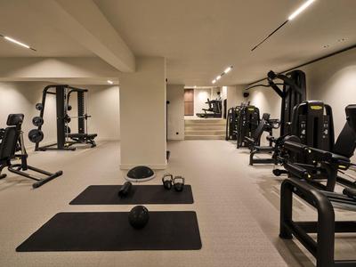 Moderner Fitnessraum mit Trainingsgeräten und Yogamatten, gut beleuchtet und geräumig.