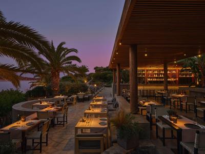 Terrasse eines Hotels mit gedeckten Tischen und Palmen bei Abenddämmerung.