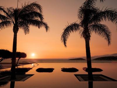 Sonnenuntergang mit Palmen und Infinity-Pool am Meer