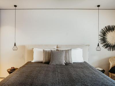 Nowoczesny pokój hotelowy z dużym łóżkiem, szarą narzutą i stylową dekoracją ściany.