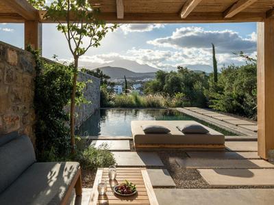 Overdekt terras met bank en uitzicht op zwembad en bergen bij zonsondergang.