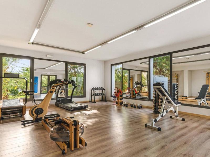 Lichte en ruime hotelgym met moderne fitnessapparatuur en grote ramen met uitzicht op groen.