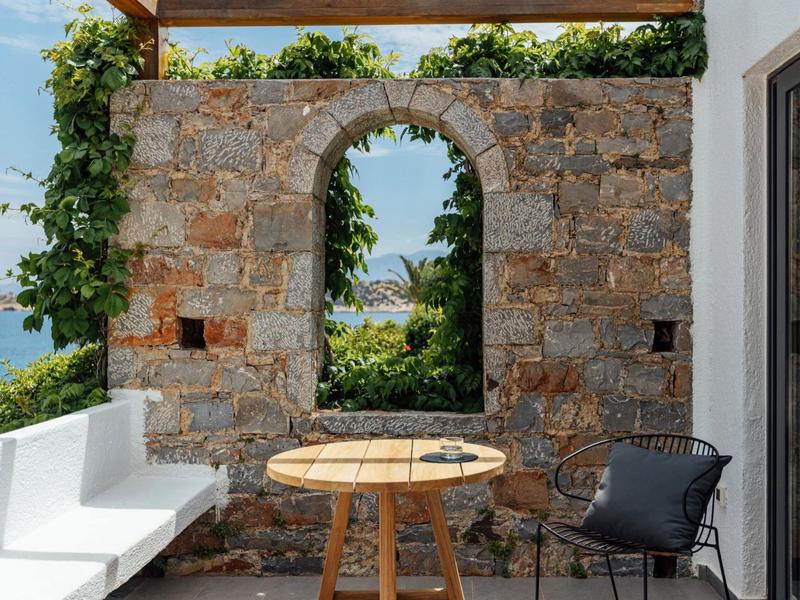 Terras met wit en zwart zitmeubilair voor een stenen muur met boog en zeezicht