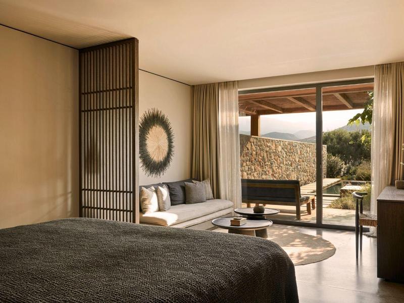 Moderne hotelkamer met groot bed, bank en terras met uitzicht op de natuur.