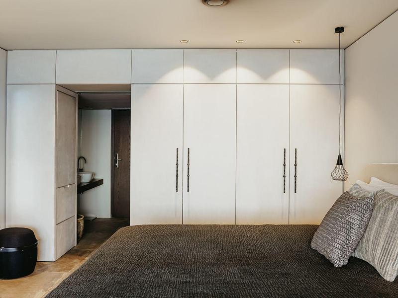 Moderne slaapkamer met groot bed, ingebouwde kledingkast en open badkamer.