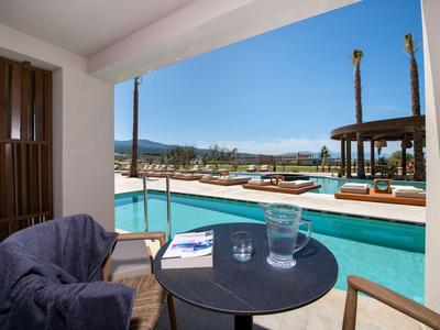 View of a pool with loungers and a table with two glasses on a terrace.