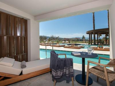 View from a hotel room overlooking a pool area with loungers and a table with two chairs.