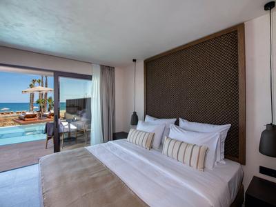 Modern hotel room with large bed and view of pool and sea.