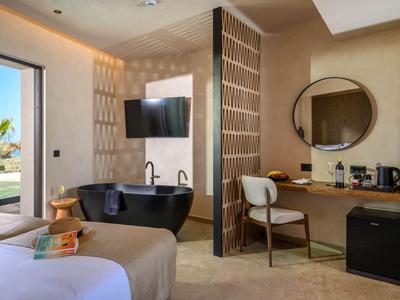 Modern hotel room with freestanding bathtub, TV, desk, and sea view.