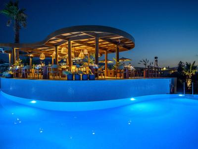 Restaurante moderno con piscina iluminada por la noche en un complejo hotelero.