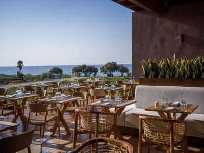 Restaurante al aire libre con sillas de mimbre y vista al mar en un día soleado.