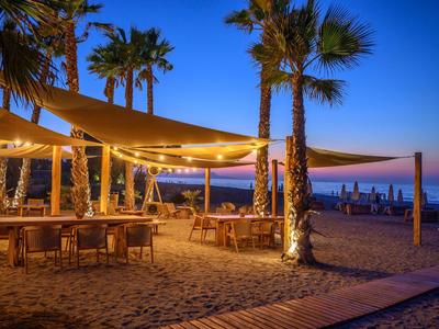 Beach restaurant with lit seating areas and palm trees at sunset.