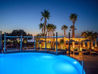 Lit pool with palm trees and seating areas at sunset in a hotel setting.