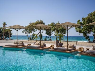 Área de piscina lujosa con tumbonas y sombrillas con vistas al mar y al cielo.