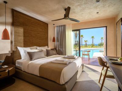 Habitación de hotel moderna con cama grande, escritorio y vista a la piscina y palmeras.
