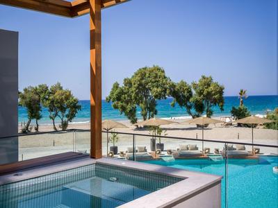 Piscina exterior moderna con jacuzzi con vistas al mar y la playa bajo un cielo azul.