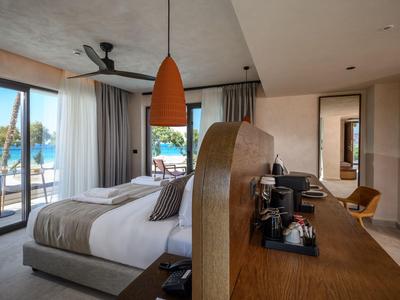 Habitación de hotel moderna con cama, escritorio grande y vista a la piscina y el mar.