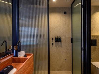 Baño moderno en hotel con ducha, lavabo de madera y colores apagados.