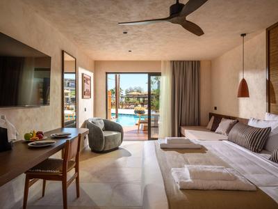 Habitación de hotel luminosa con cama grande, escritorio y vista a la piscina a través de puerta acristalada.