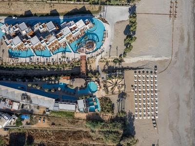 Vista aérea de un hotel con piscinas y tumbonas en la playa junto al mar.