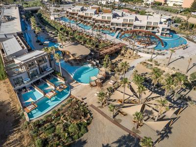 Resort hotelero de lujo con varias piscinas, terrazas al sol y palmeras junto a una playa de arena.