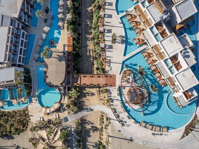 Vista aérea de un hotel con dos piscinas, tumbonas y caminos en un entorno tropical.